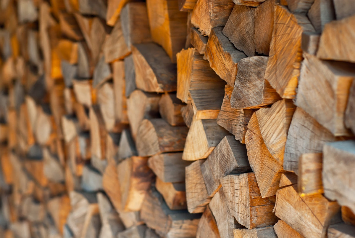 A close-up view of stacked firewood logs with visible grain, bark, and cut ends, filling the frame.